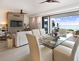 Una sala de estar moderna con una mesa de vidrio, sofás blancos y vista al océano.