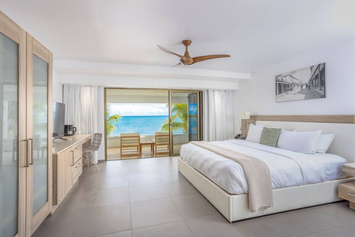 Quarto de hotel com cama, escrivaninha, poltrona, cafeteira e vista para o mar.