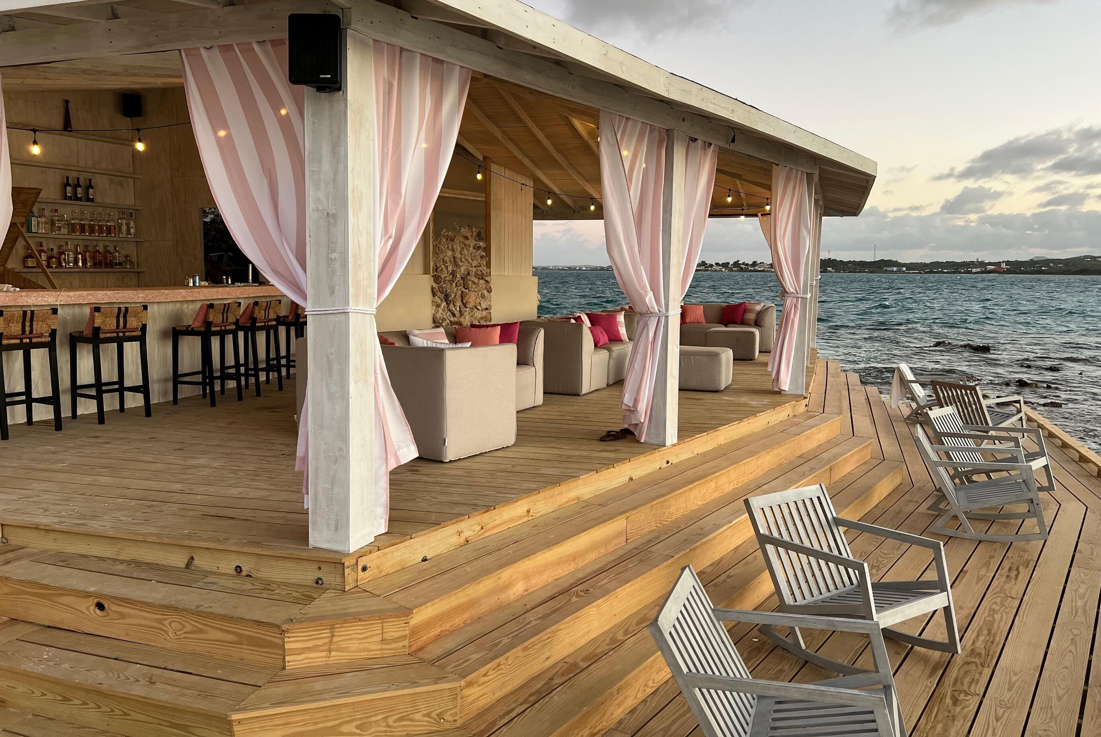 A wooden deck with outdoor seating and a bar area overlooking the water.