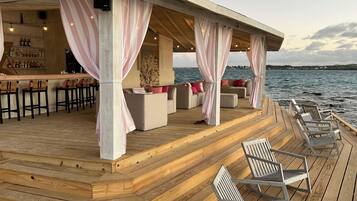 Um deck de madeira com área de estar ao ar livre e bar, com vista para a água.