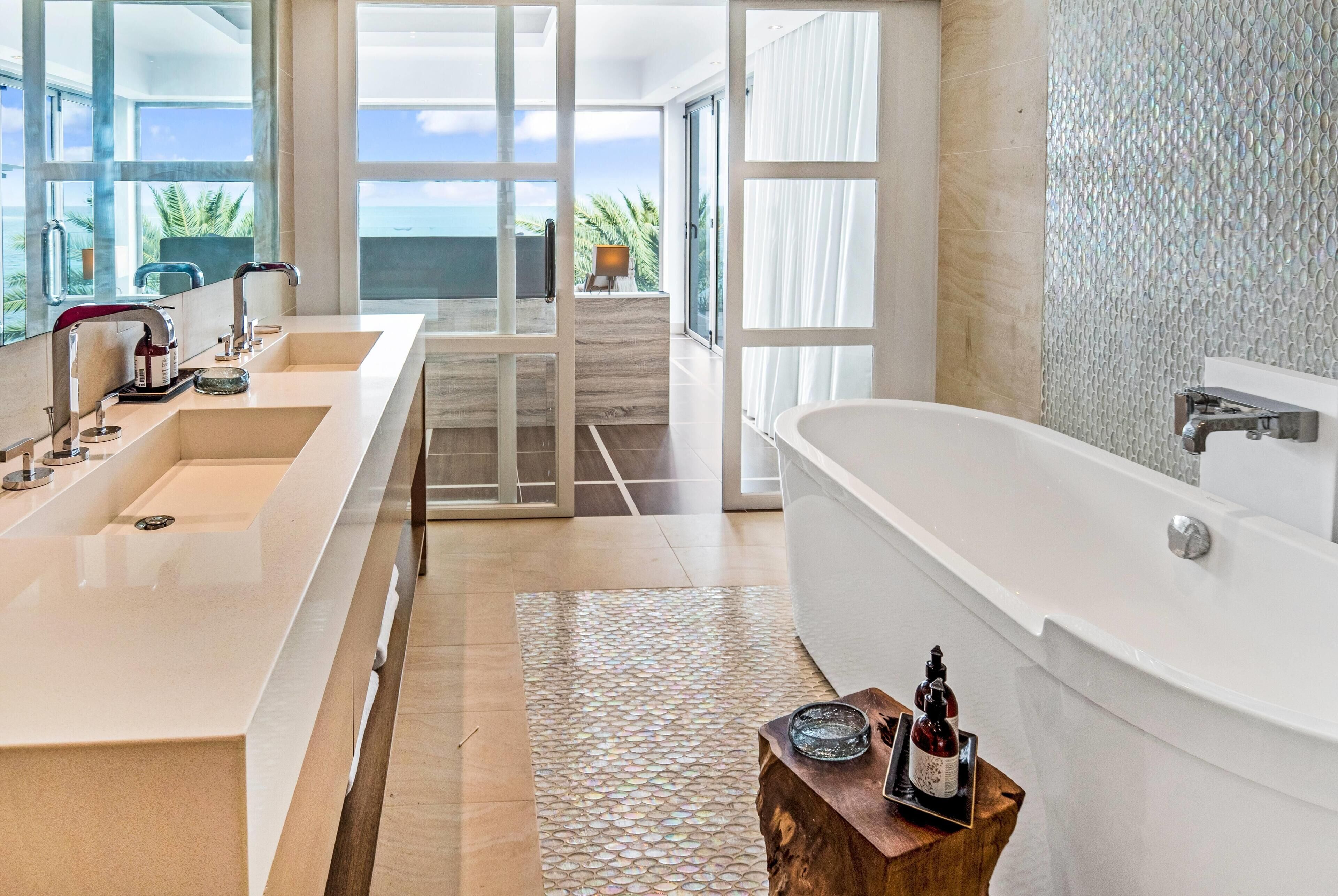 Un baño moderno con una bañera grande, dos lavamanos y vistas al océano a través de amplios ventanales.
