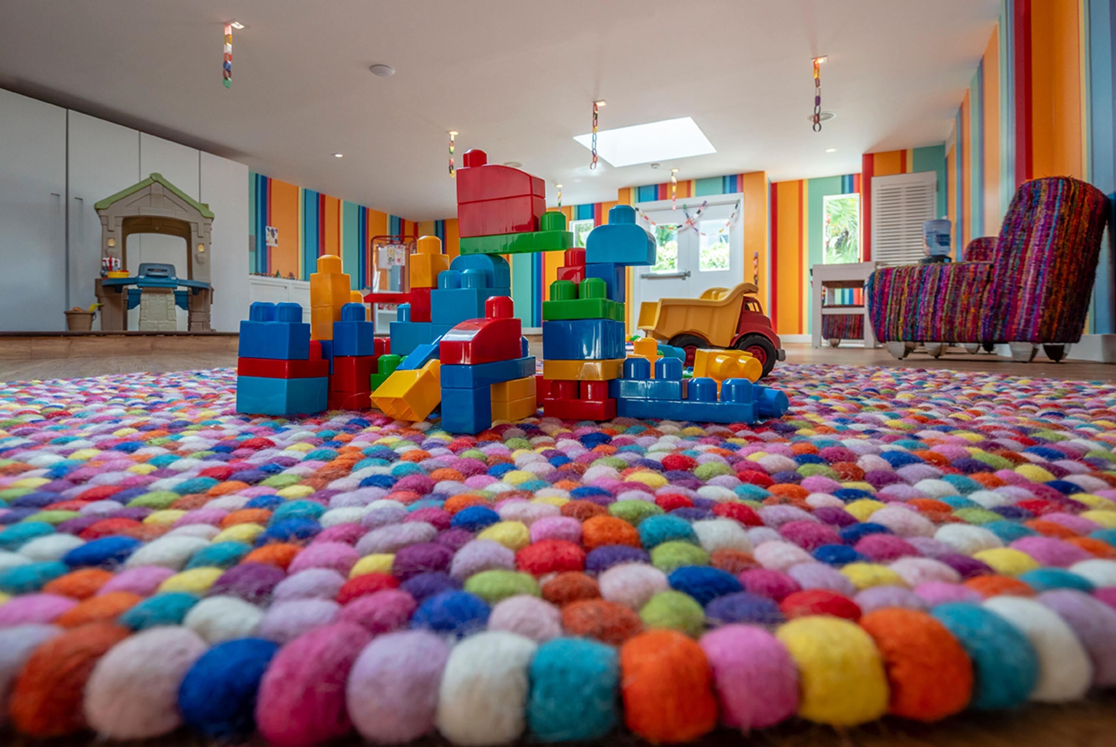 A playroom with colorful building blocks, a playhouse, and a colorful shag carpet.
