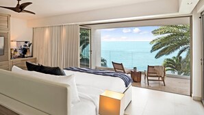 Une chambre d’hôtel avec un grand lit, un bureau avec une lampe, une télévision et un balcon offrant une vue sur l’océan.