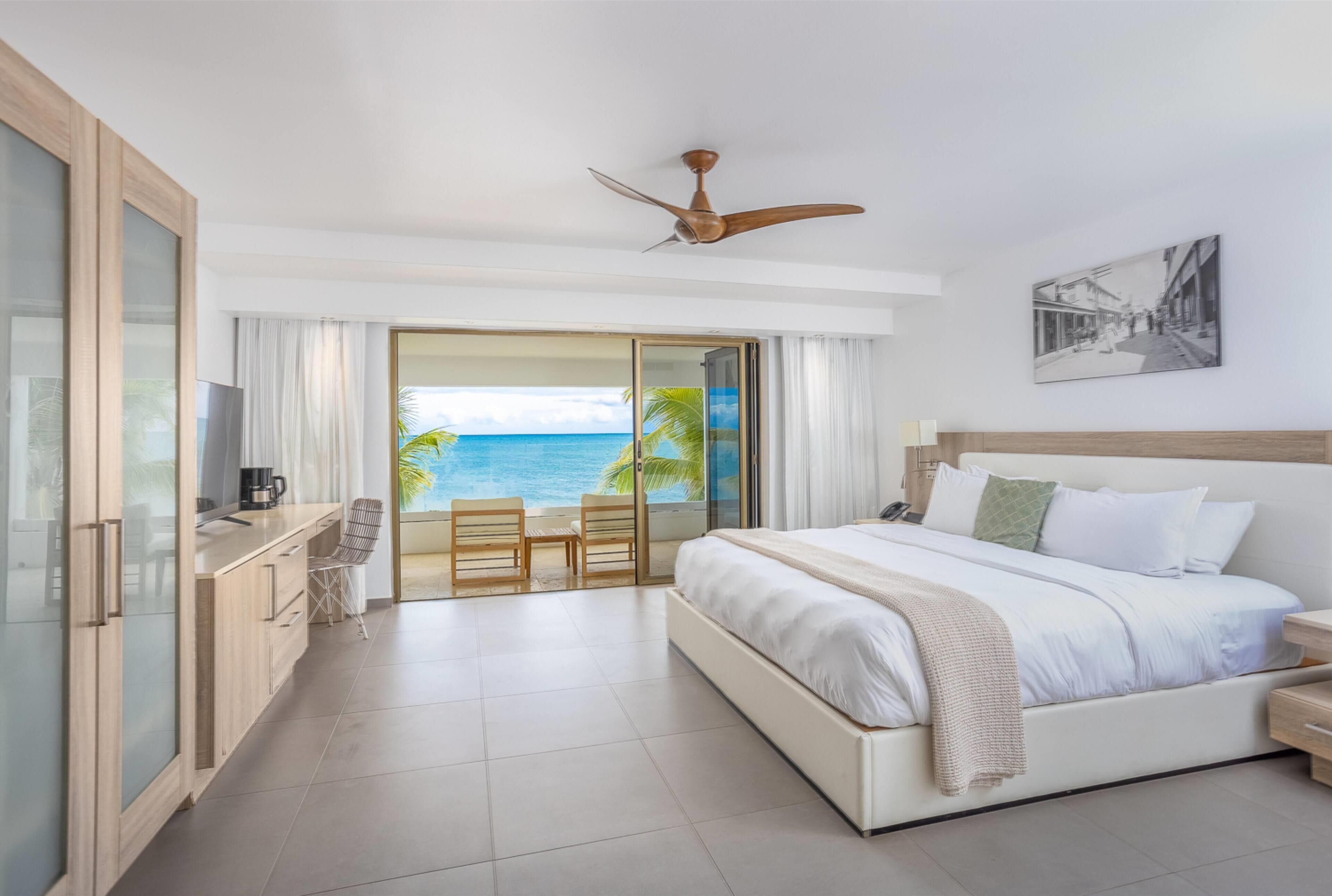 A hotel room with a bed, a TV, a coffee maker, a desk, and a view of the ocean.