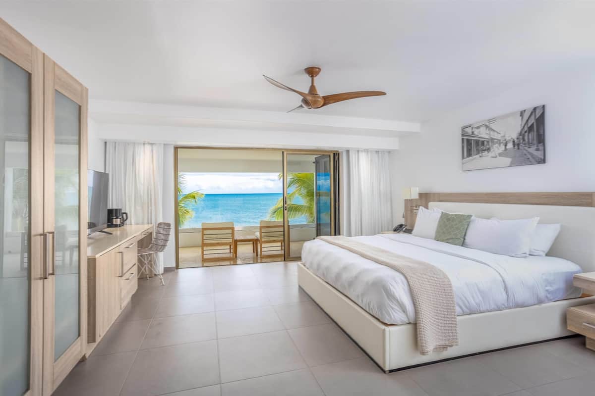 A hotel room with a bed, a TV, a coffee maker, a desk, and a view of the ocean.