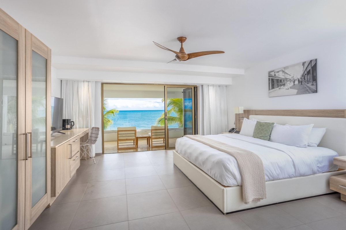 A hotel room with a bed, a TV, a coffee maker, a desk, and a view of the ocean.