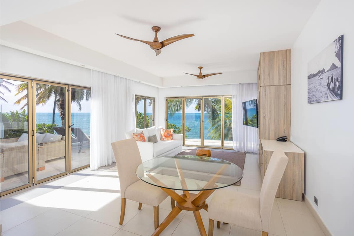 A spacious living area with a glass table, comfortable seating, ceiling fans, and large windows offering ocean views.