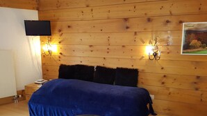 Une chambre avec un mur en bois, un lit recouvert d’une couverture bleue, deux lampes fixées au mur, un téléviseur à écran plat et un tableau.