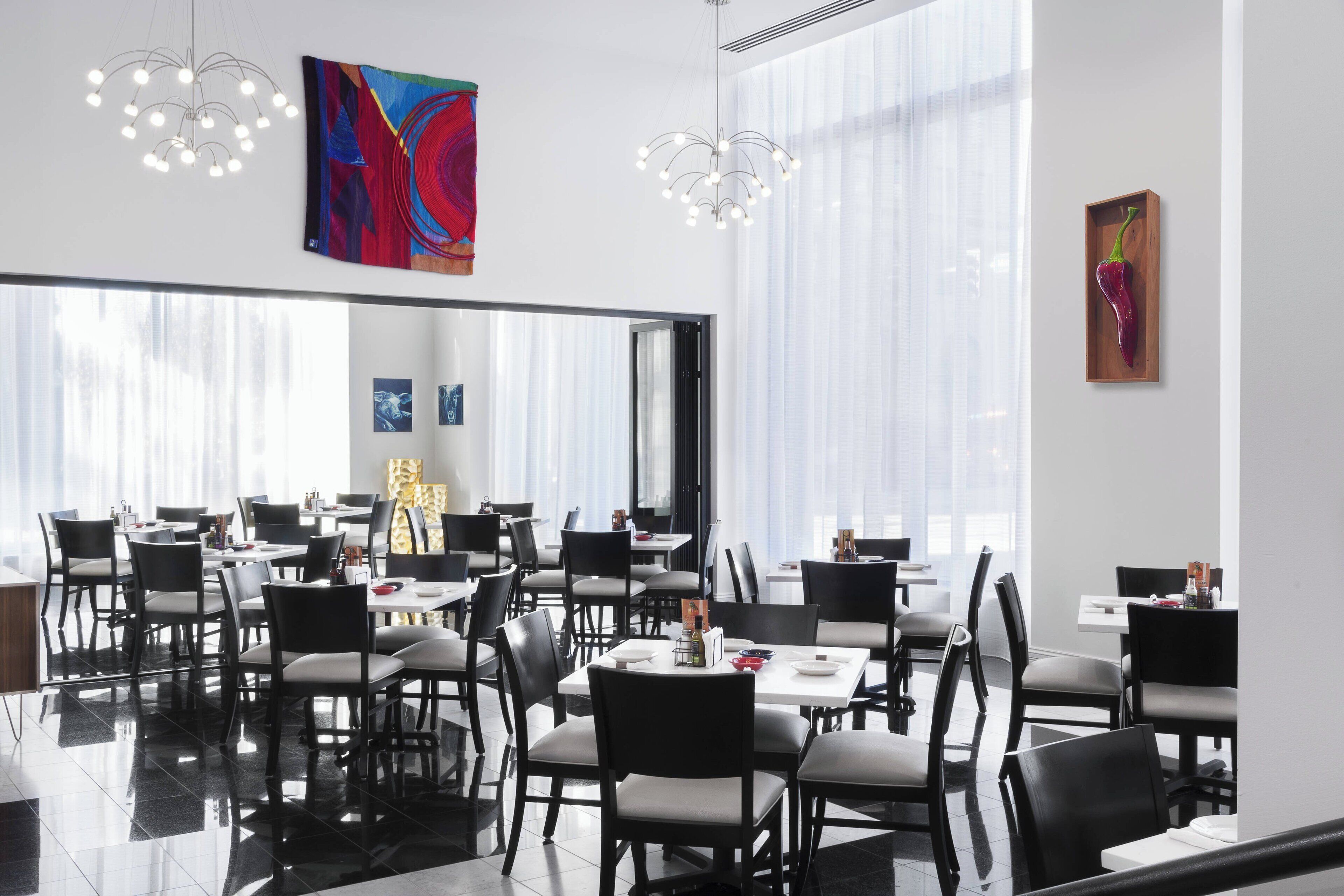 Un'area pranzo moderna con sedie nere e tavoli bianchi, ampie finestre e opere d'arte contemporanee alle pareti.