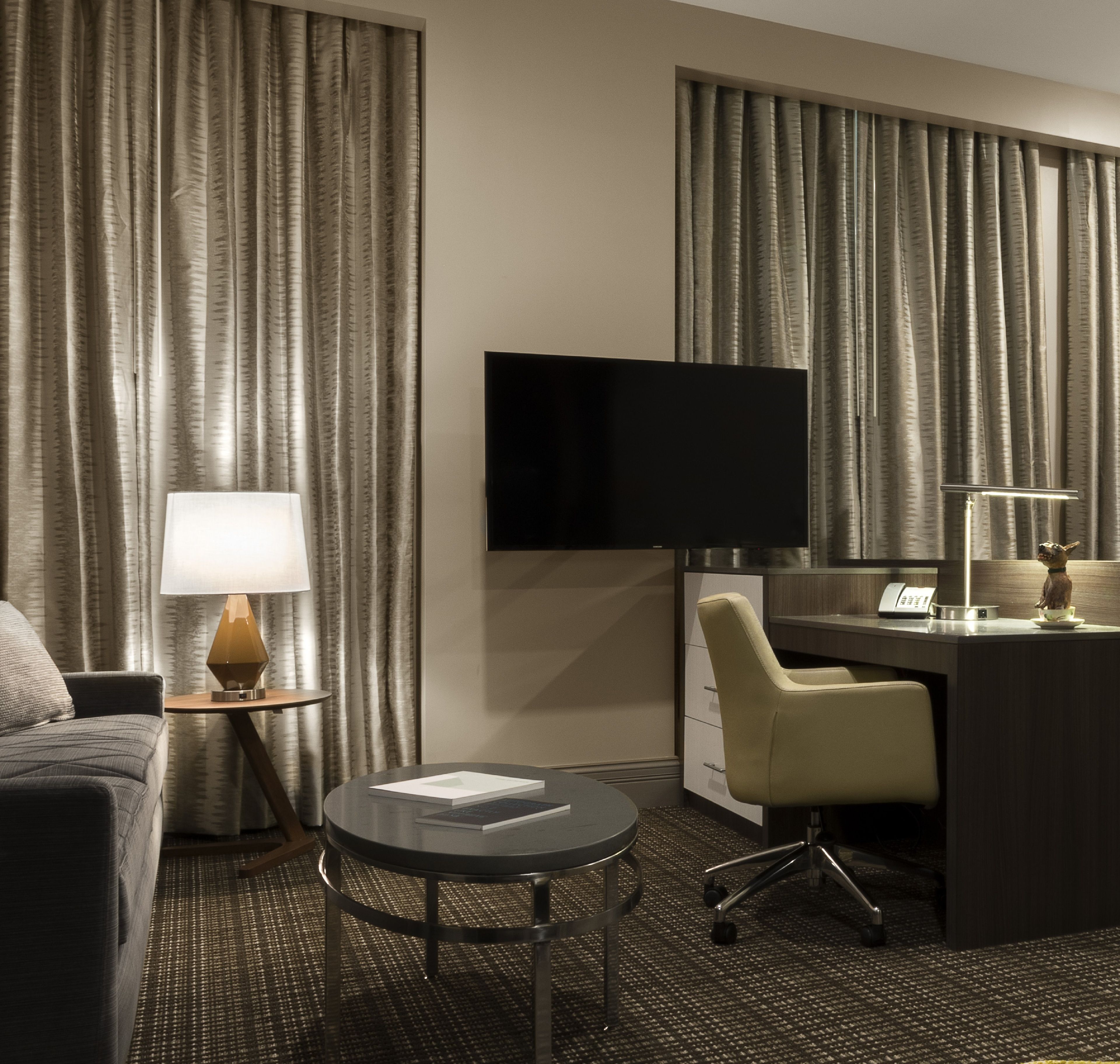 A hotel room with a bed, a desk, a chair, a television, and a lamp.