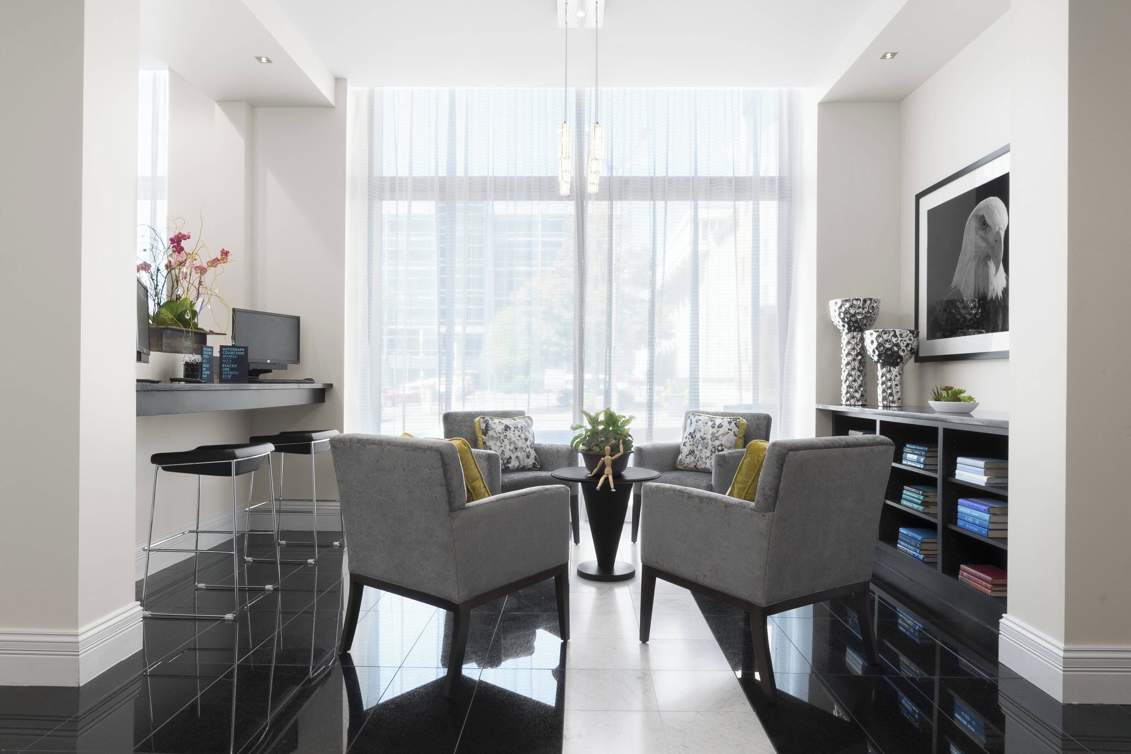 A modern living room with a large window, two grey armchairs, a black coffee table, a TV on a shelf, and a bookshelf with books and decorative items.