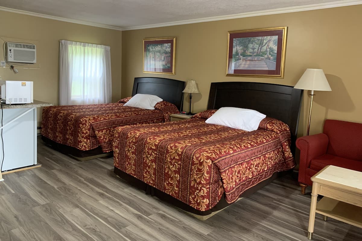 A hotel room with two beds, a desk, a chair, and a lamp.