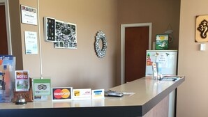 A reception desk with a wooden counter, a hanging light fixture, and various informational signs including a welcome sign and a membership certificate. - Dunlop Motel (Ashfield-Colborne-Wawanosh)