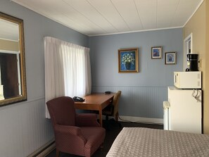 Ein Hotelzimmer mit einem Bett, einem Schreibtisch mit Stuhl, einem Telefon, einer Kaffeemaschine und einem Bild an der Wand.