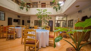 A spacious indoor area with multiple round tables and chairs, a central plant, and a balcony with railings. - Chester Hotel (Nakuru)