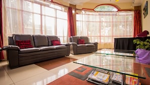 A living room with a sofa, armchair, glass coffee table, and a potted plant. - Chester Hotel (Nakuru)