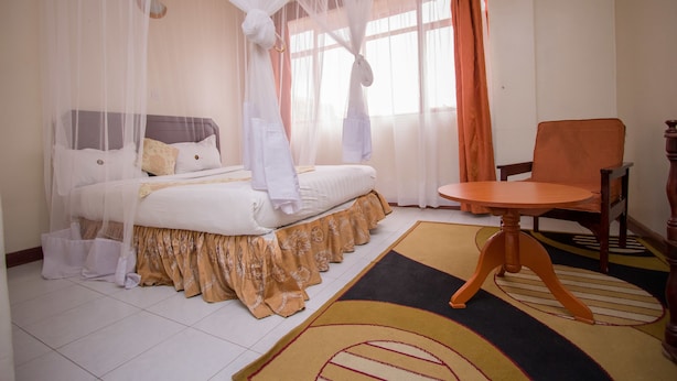 A bedroom with a bed, a chair, and a window with curtains. - Chester Hotel (Nakuru)