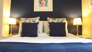 A neatly made bed with a blue blanket, two matching pillows, and a framed artwork above. - Moortown Lodge 1760 (Ringwood)