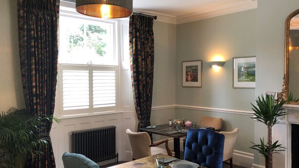 A dining area with a table set for four, a blue upholstered chair, a potted plant, and a fireplace. - Moortown Lodge 1760 (Ringwood)