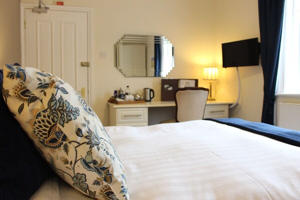 A hotel room with a bed, a desk with a chair, a television, and a window with curtains. - Moortown Lodge 1760 (Ringwood)