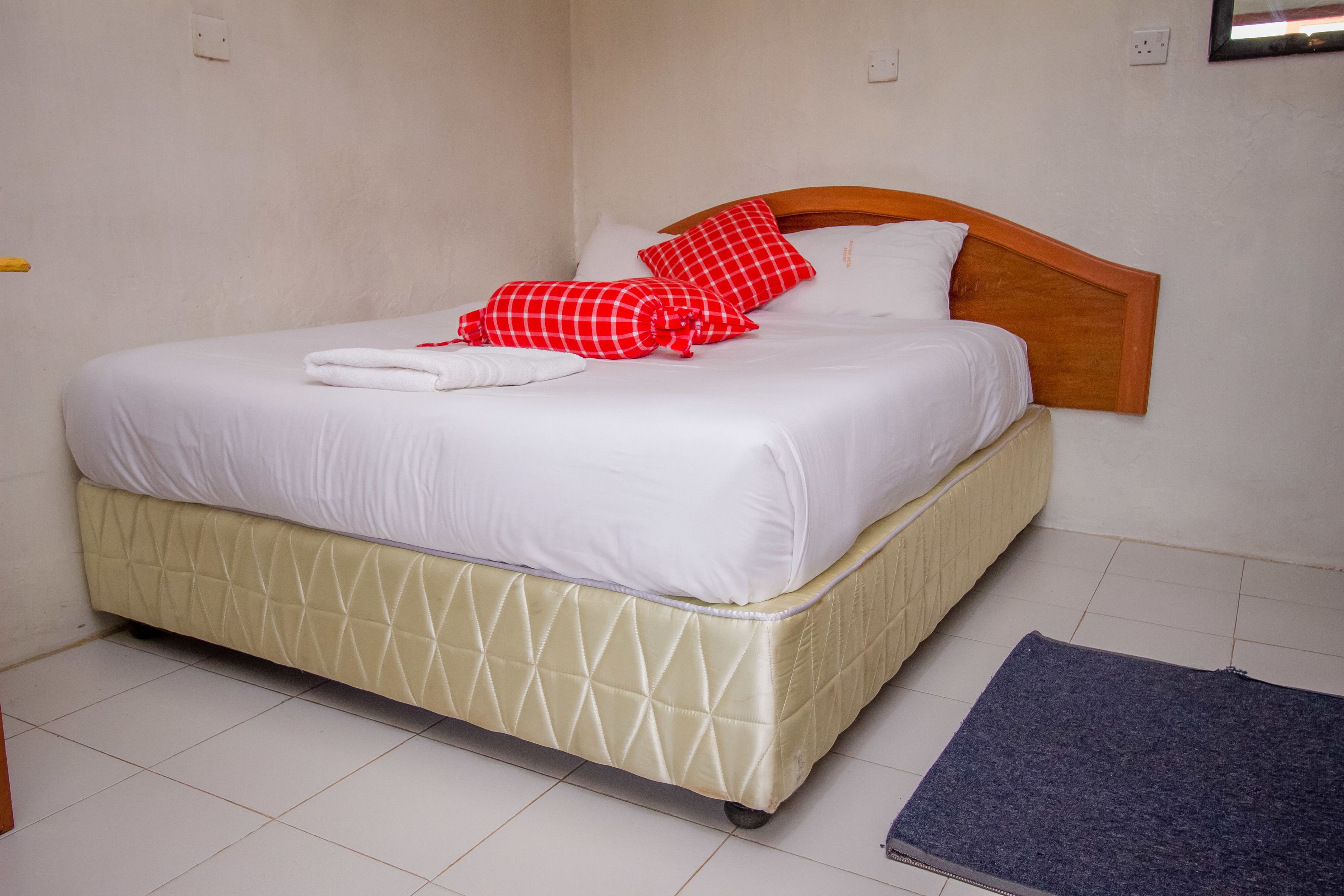 A neatly made bed with white linens and red checkered pillows, a wooden headboard, and a quilted mattress cover.