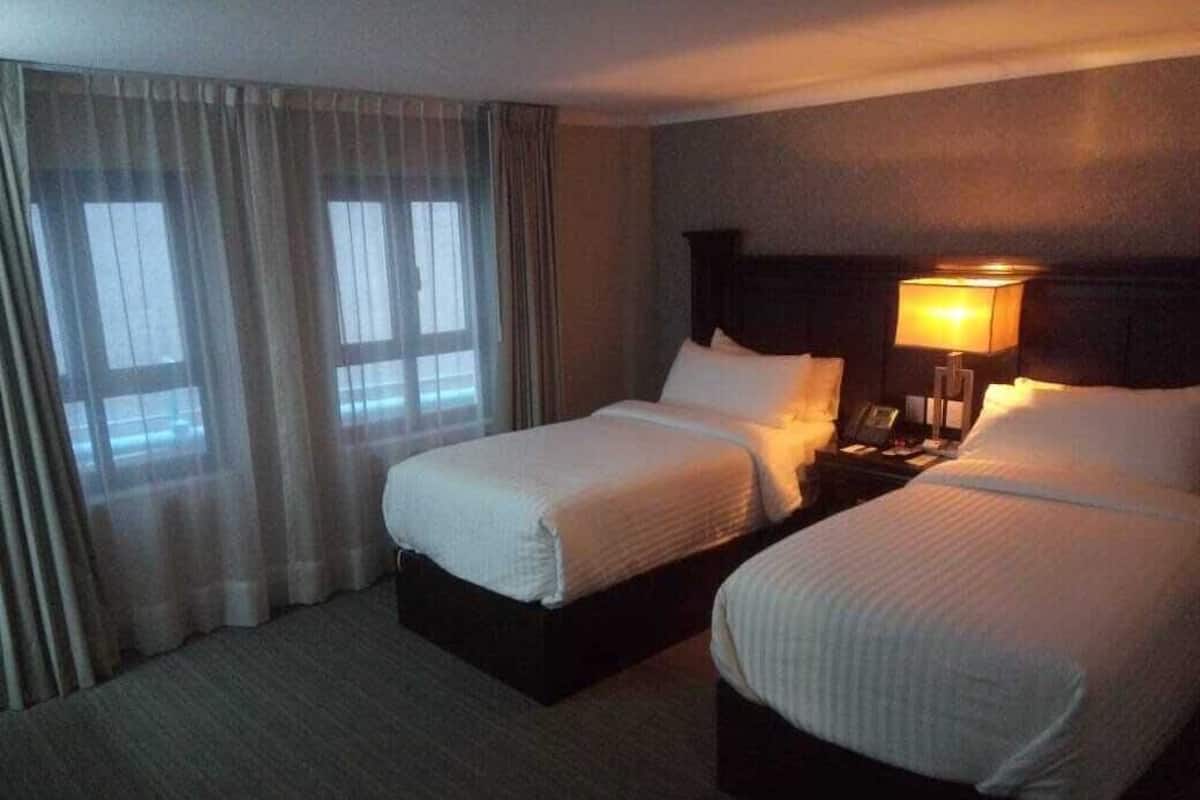 A hotel room with two beds, a nightstand with a lamp, and a window with curtains.