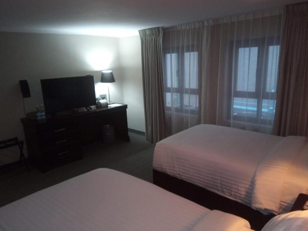 Quarto de hotel com duas camas, televisão, escrivaninha e abajur.