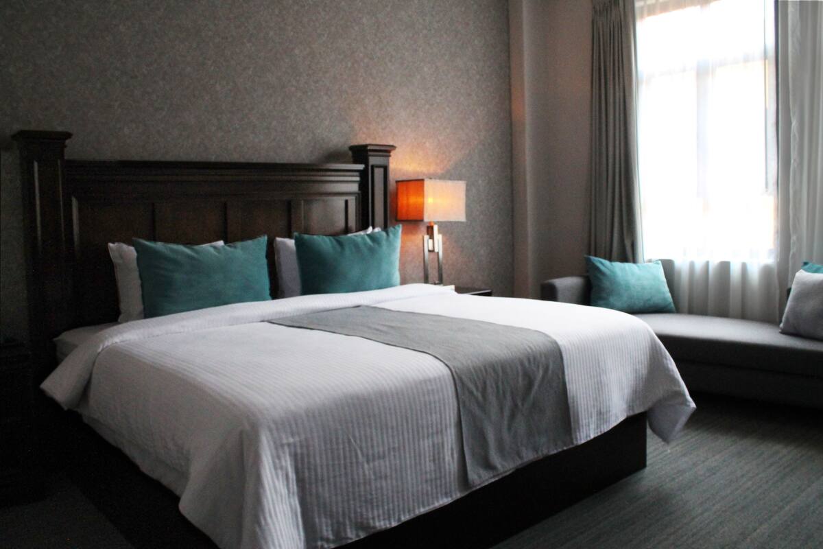 A hotel room with a large bed, a nightstand, a lamp, and a window with curtains.