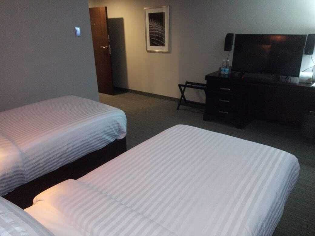 Habitación de hotel con dos camas, un escritorio, una silla y un televisor.