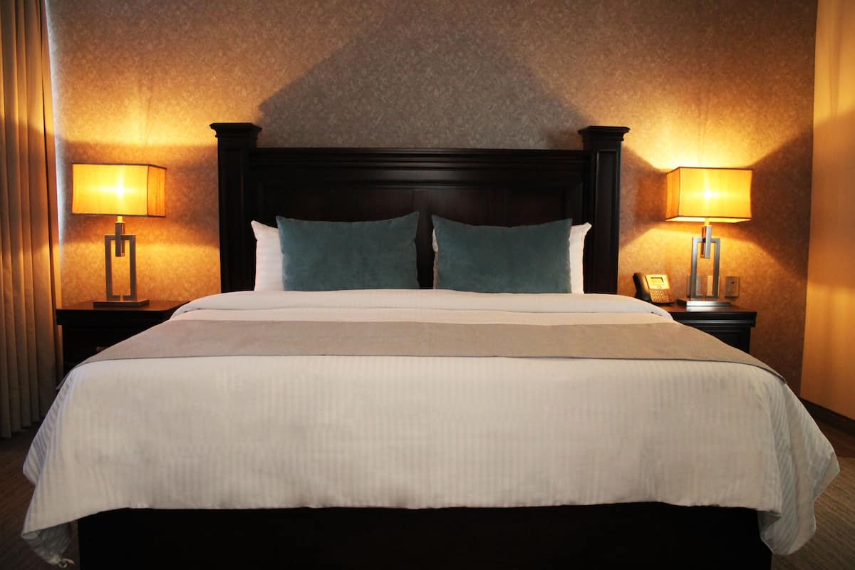 A hotel room with a large bed, two bedside tables, and two lamps.