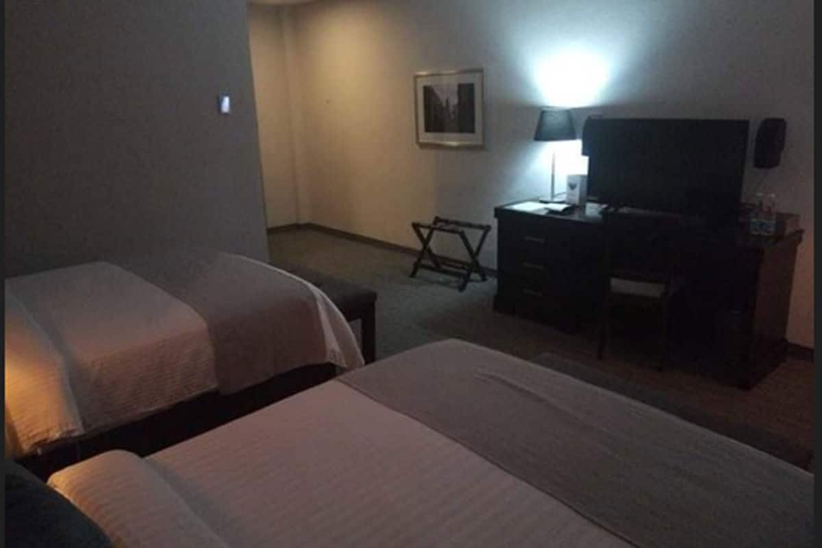 A hotel room with two beds, a desk with a chair, a lamp, and a television.
