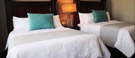 Dos camas individuales con cabeceros de madera, ropa de cama blanca y almohadas color aguamarina.