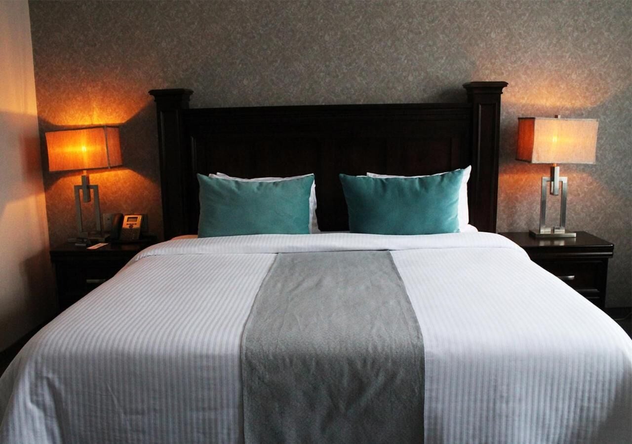 A neatly made bed with a dark headboard, two pillows, and a bedside table with a lamp.