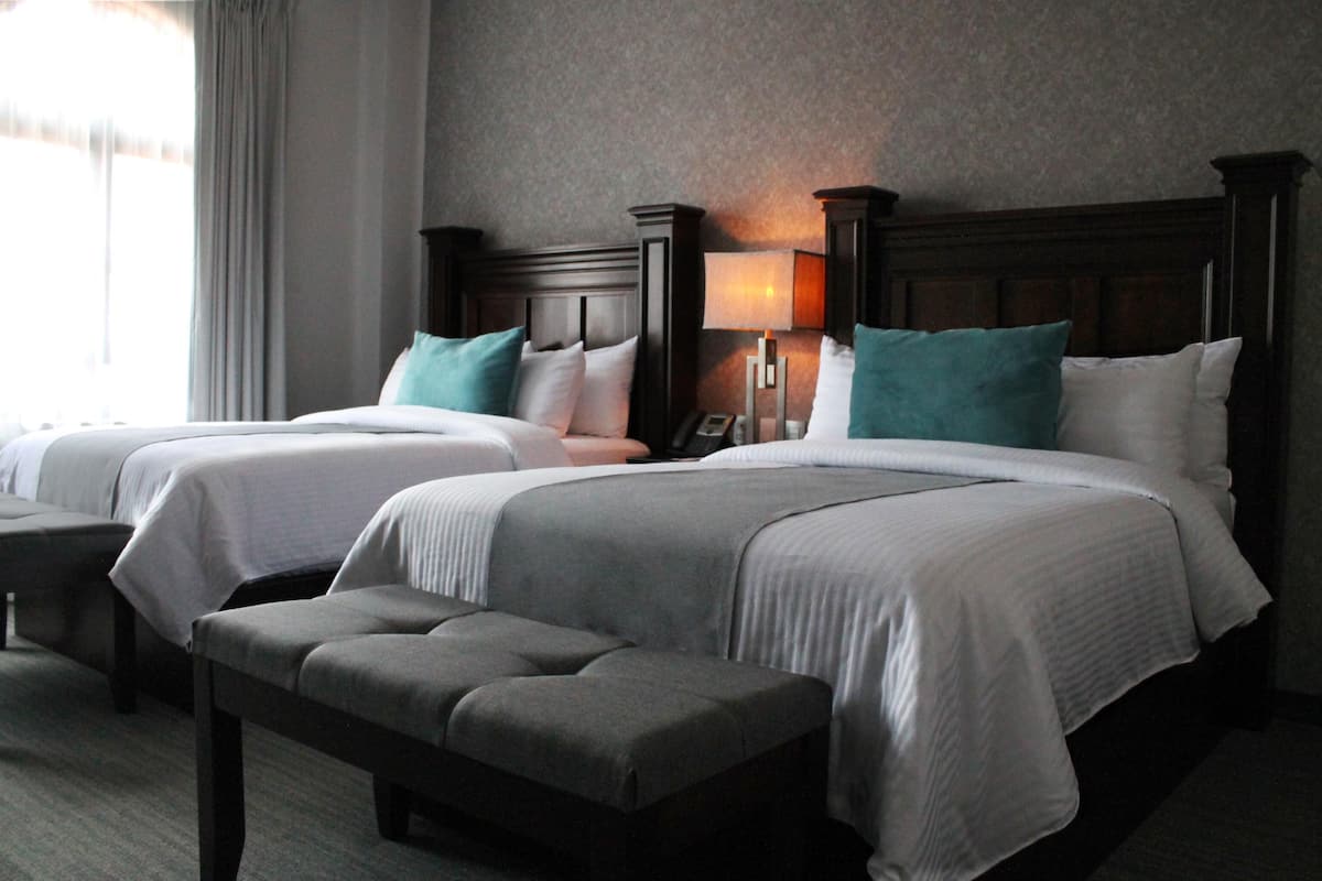 A hotel room with two beds, a bench, and a lamp.