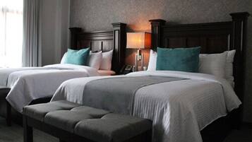 Una habitación de hotel con dos camas, un banco y una mesita de noche con lámpara.