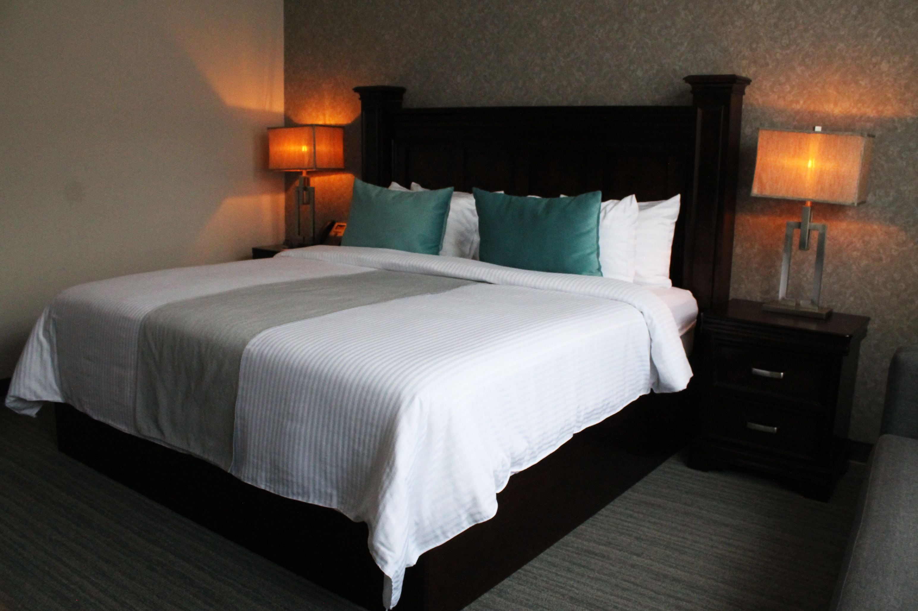 A hotel room with a large bed, two bedside tables with lamps, and a dark headboard.