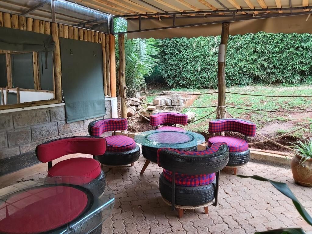 An outdoor seating area with chairs and tables made from tires, a covered roof, and a view of a garden with trees and a brick wall.