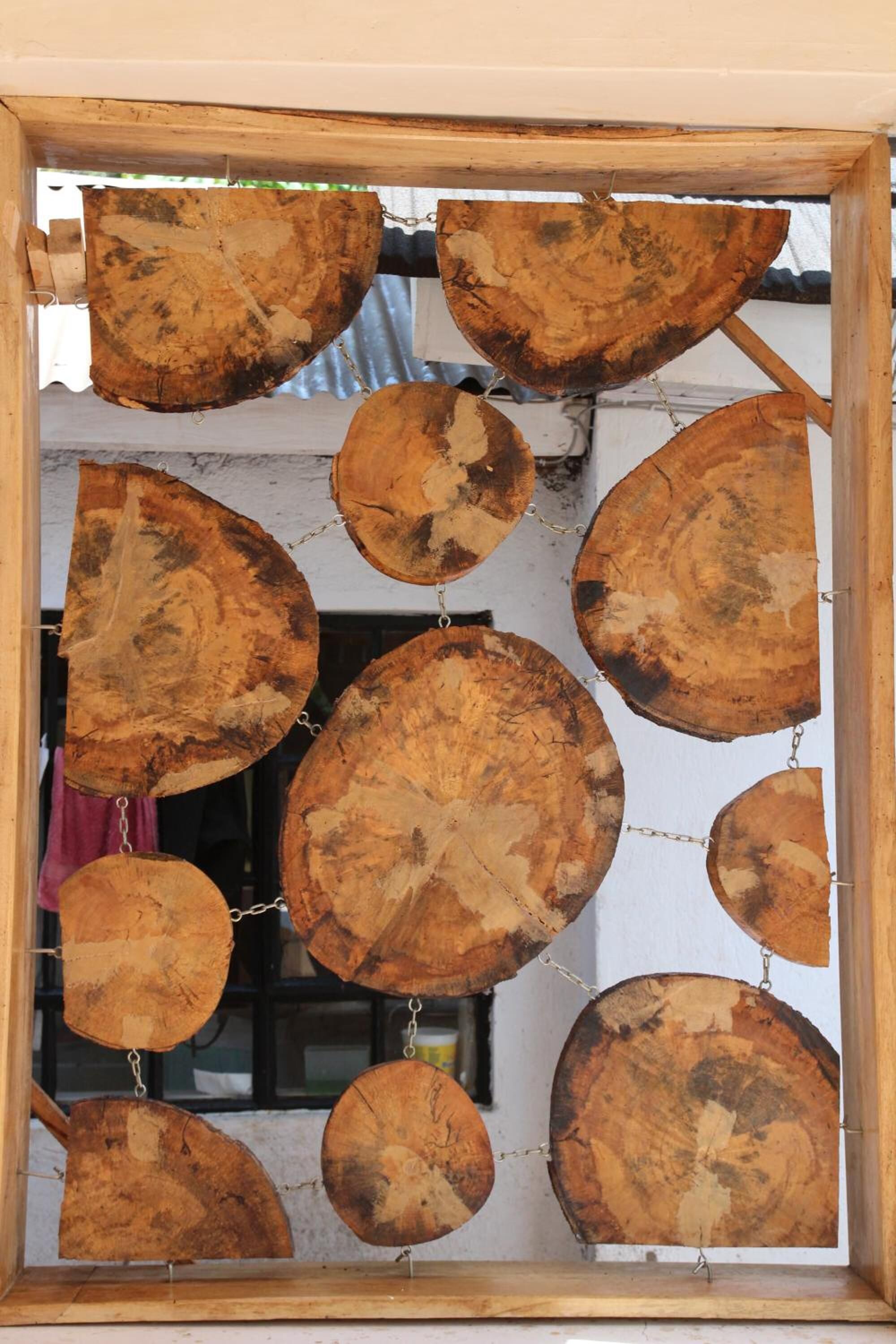 Moldura de janela de madeira com peças circulares de madeira penduradas no interior, possivelmente para decoração ou artesanato.