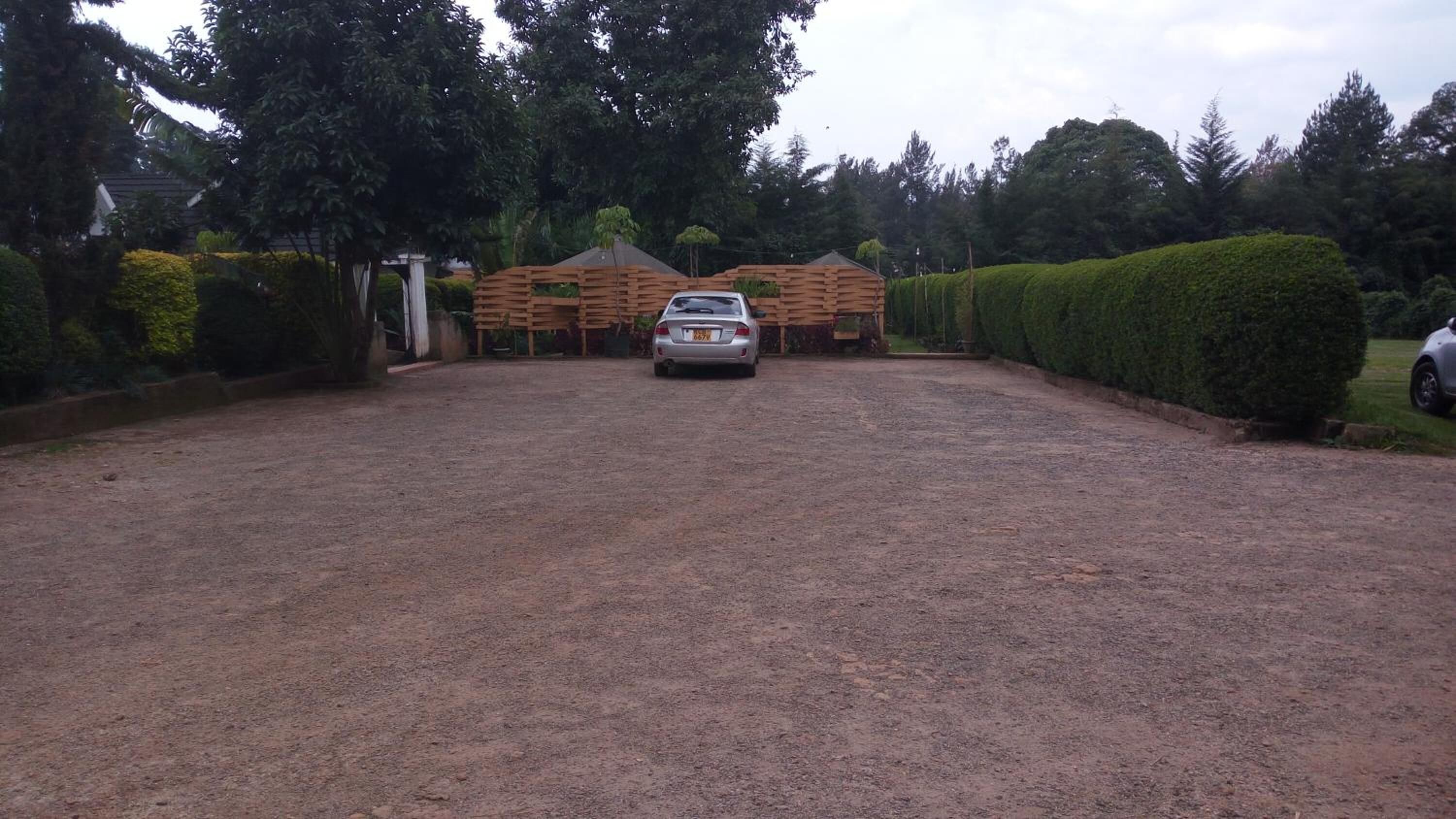 A gravel driveway leading to a building with a wooden fence and a car parked in front.