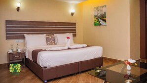 Una habitación de hotel con una cama grande, una mesita de noche, una mesa de centro de vidrio y un cuadro en la pared.
