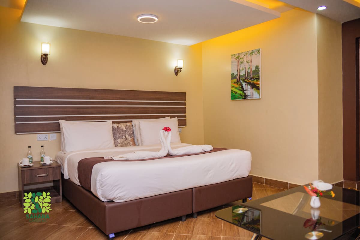 A hotel room with a large bed, a nightstand, a glass coffee table, and a painting on the wall.