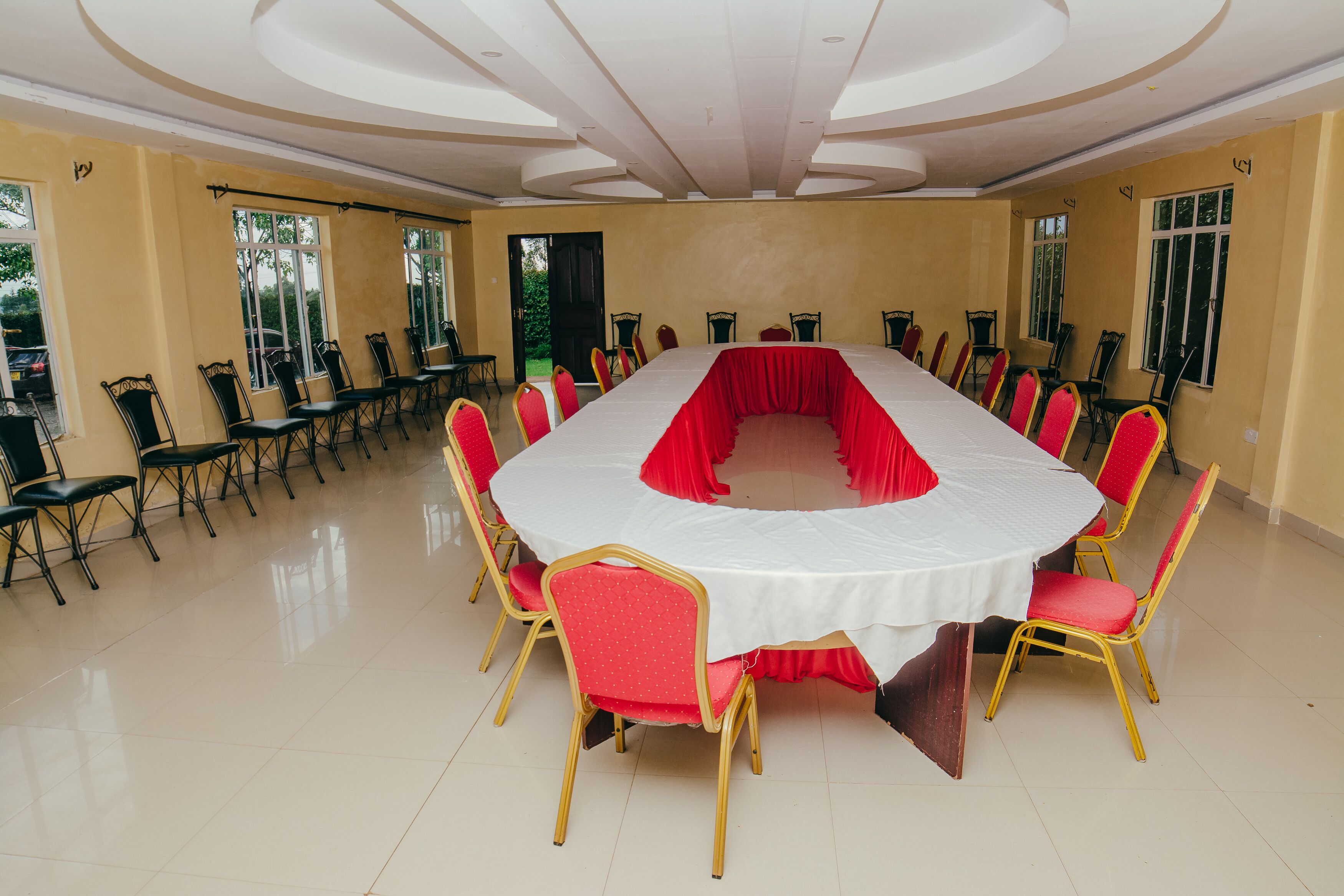 A conference room with a long table surrounded by red and gold chairs, large windows, and a high ceiling.