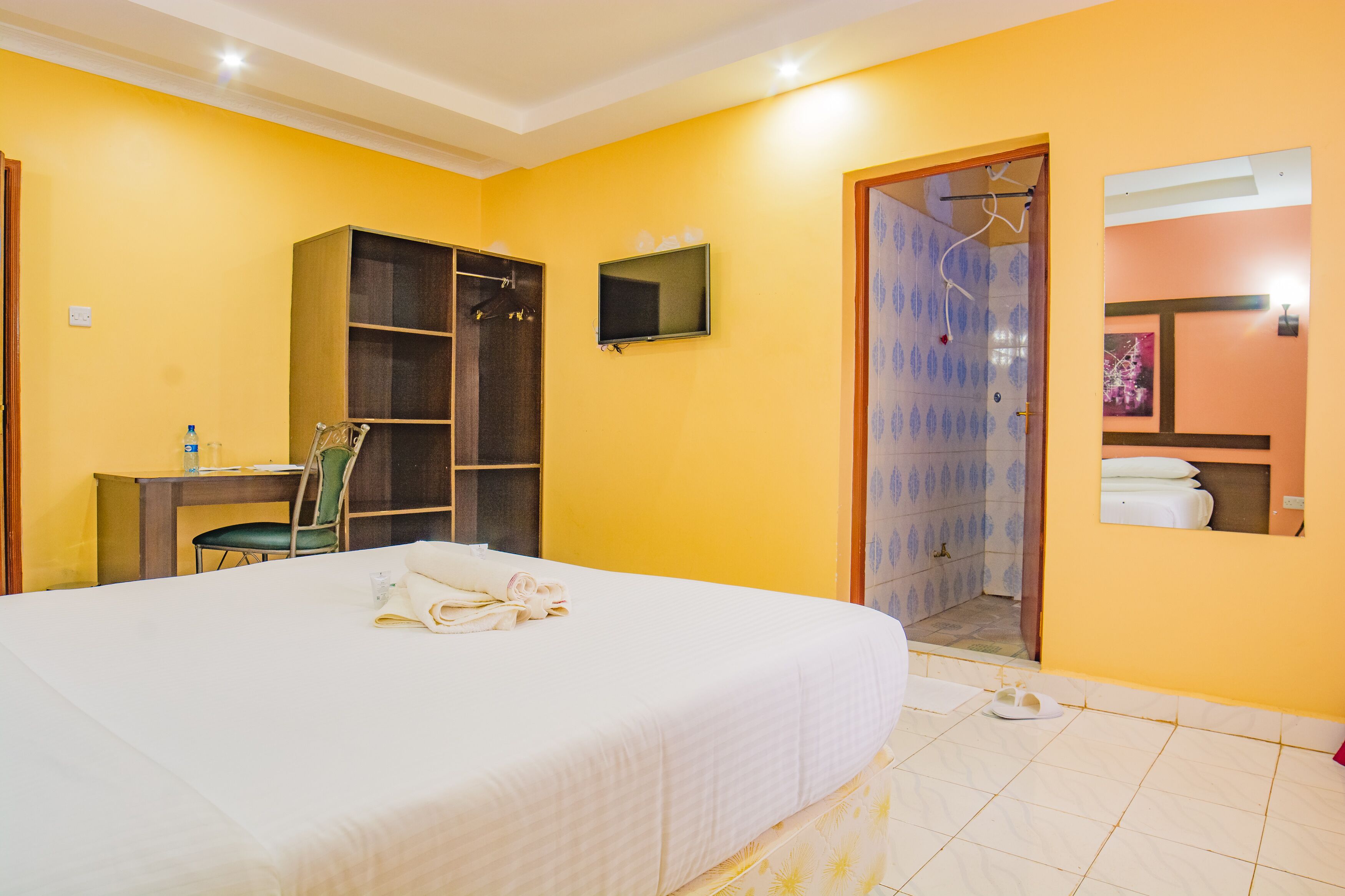 A hotel room with a bed, a desk, a chair, a wardrobe, a shower area, and a small bathroom.