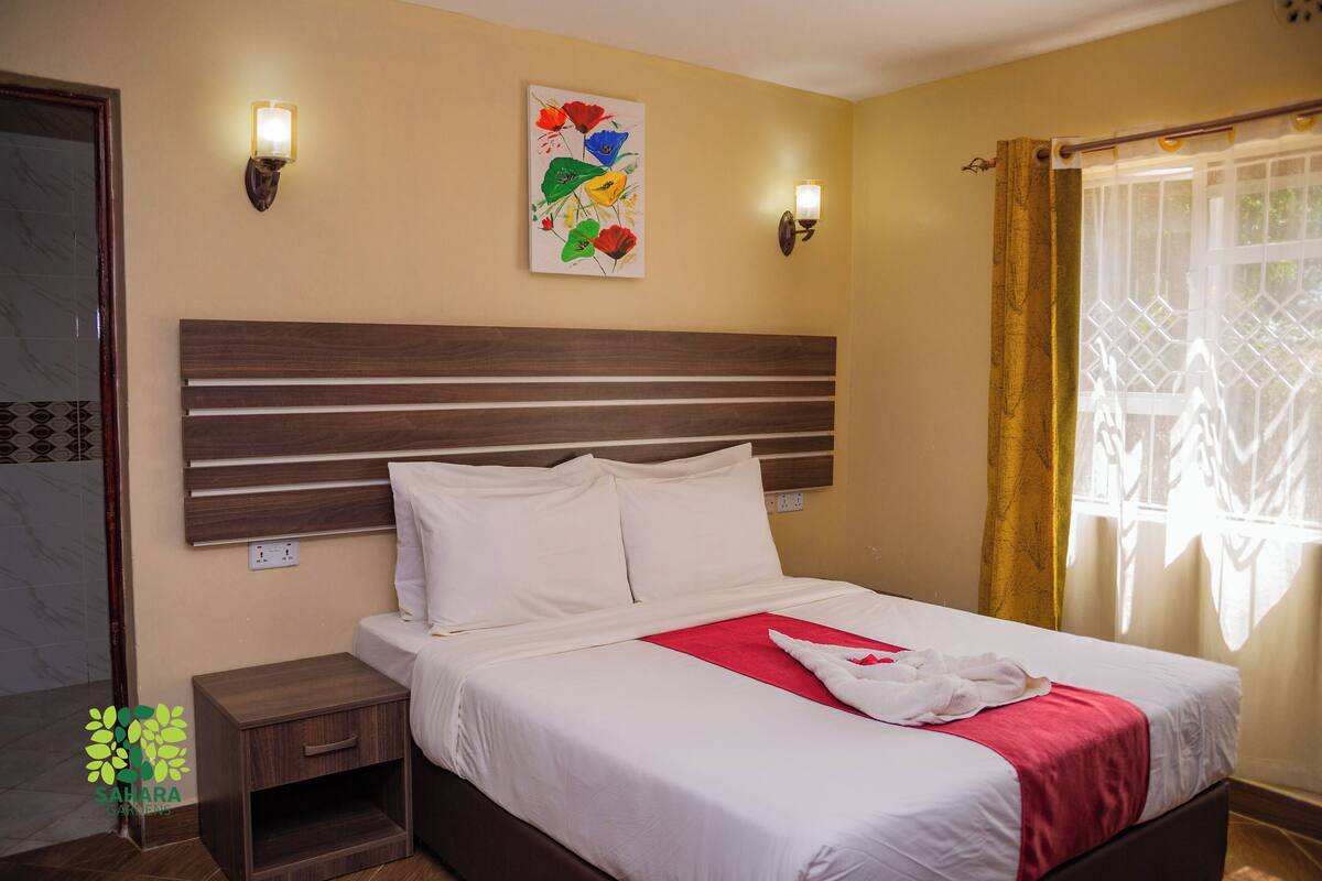 A hotel room with a bed, nightstands, a wall-mounted light fixture, and a window with curtains.