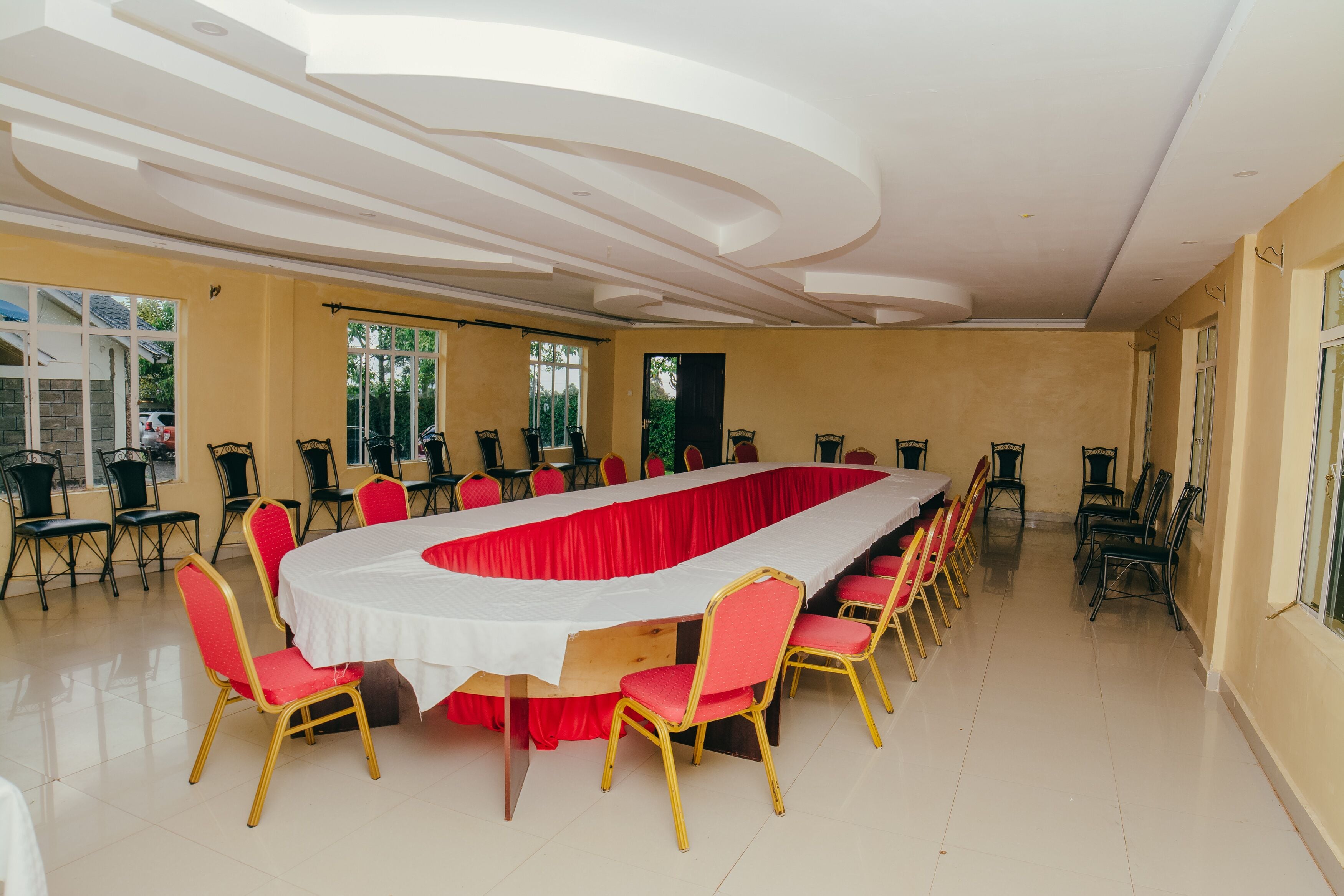 Een vergaderzaal met een lange tafel, rode en gouden stoelen en een wit plafond.