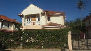 A two-story house with a balcony, surrounded by lush greenery and a gated entrance. - Azanza Mtwapa Holiday Home (Mtwapa)