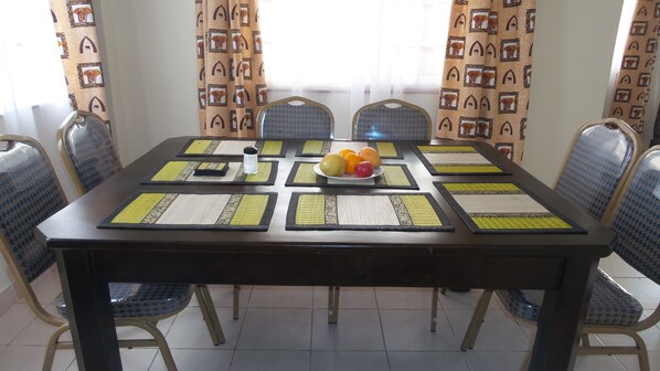 A dining table with placemats, a fruit bowl, and chairs.