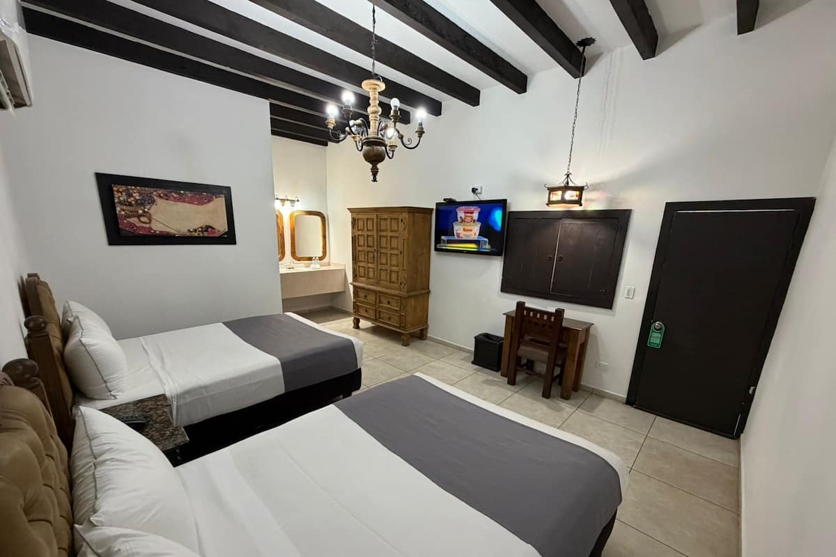 A hotel room with two beds, a wooden cabinet, a television, and a door.