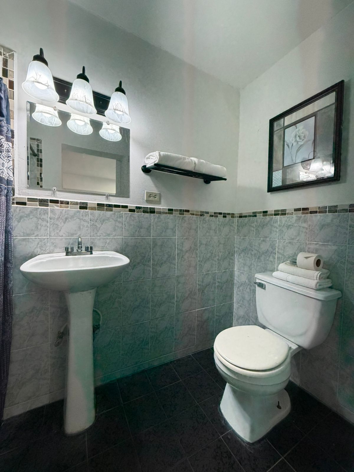 A bathroom with a pedestal sink, a toilet, and a mirror with lights.