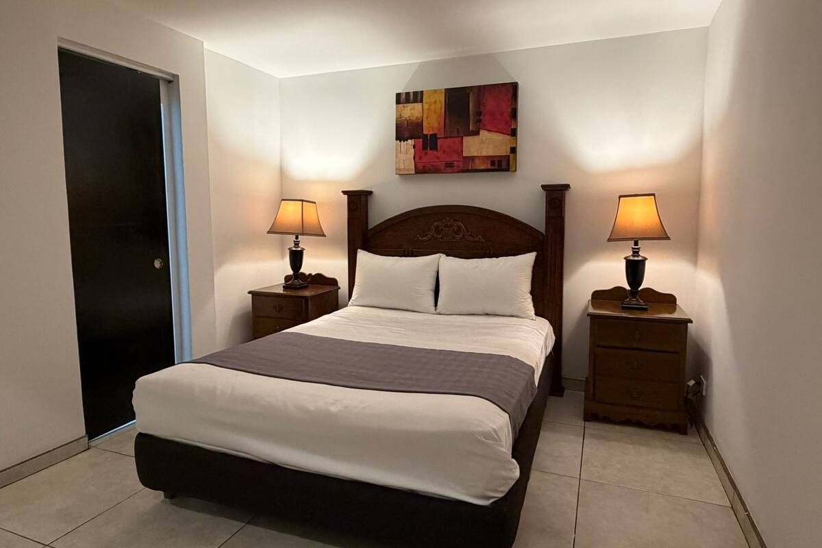 A hotel room with a bed, two bedside tables with lamps, a door, and a wall-mounted artwork.
